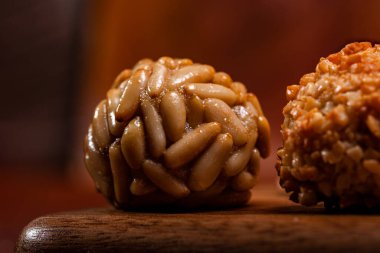 Çam fıstığıyla kaplanmış geleneksel panellere yakın, Castanyada için katalan tatlıları sergileniyor, sıcak sonbahar tonlarıyla kırsal ahşap bir yüzey üzerinde dinleniyor.