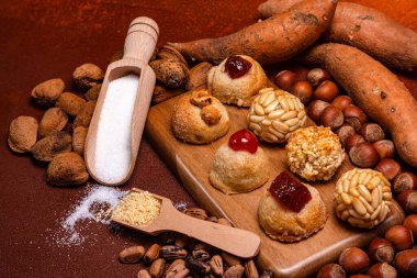 Küçük yuvarlak paneller, geleneksel katalan tatlılar, ahşap bir tahtanın üzerinde, şenlikli castanyada kutlamaları için kavrulmuş patates, badem, fındık, çam fıstığı ve şeker sergileniyor.