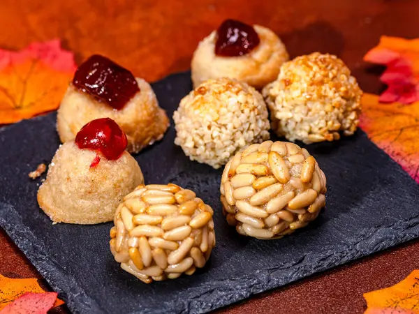 Geleneksel paneller ve çam fıstığı, şekerli meyve ve susam tohumlarıyla kaplı tatlı patatesler, bir levhada dinleniyor ve sonbahar yapraklarıyla çevrili Castanyada kutlaması için.