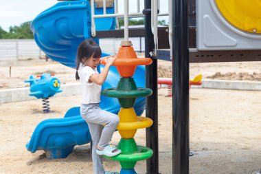 Genç bir kız gökyüzü mavisi kaydırağında oturuyor, gülümsüyor ve el sallıyor. Eğlence ve heyecan kavramı, kız çocuk parkında eğlenirken.