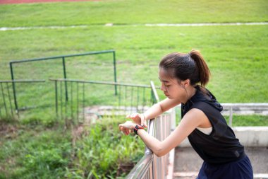 Genç bir kadın antrenman için hazırlanıyor, spor takımlarını ayarlıyor ve mesafeyi takip etmek için ukalalığını ayarlıyor, spor hedeflerini fethetmeye hazırlanırken gözleri kararlılıkla parıldıyor..