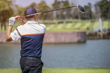 Bir adam mükemmel bir golf vuruşu yapar, kusursuz bir şekilde topa odaklanır, onu yemyeşil çimenli yolda süzülmeye hazırdır..