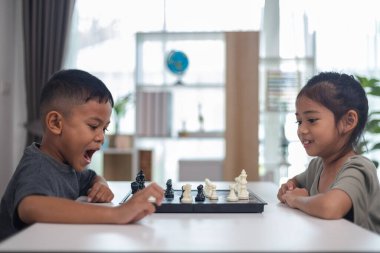 İki çocuk satranç oynuyor. Biri erkek, diğeri de bir kız. Önlerinde bir satranç tahtasıyla bir masada oturuyorlar.