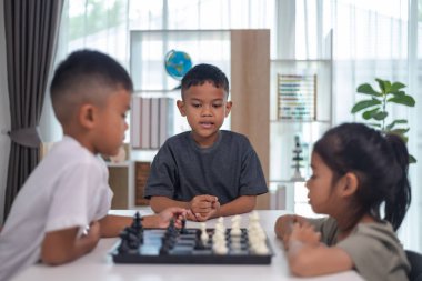 İki çocuk satranç oynuyor. Biri erkek, diğeri de bir kız. Önlerinde bir satranç tahtasıyla bir masada oturuyorlar.