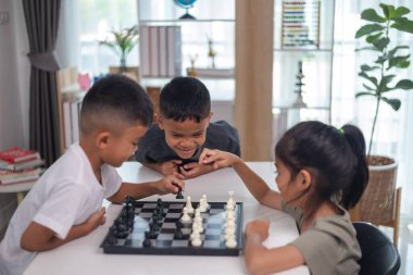 İki çocuk satranç oynuyor. Biri erkek, diğeri de bir kız. Önlerinde bir satranç tahtasıyla bir masada oturuyorlar.
