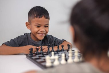 İki çocuk satranç oynuyor. Biri erkek, diğeri de bir kız. Önlerinde bir satranç tahtasıyla bir masada oturuyorlar.