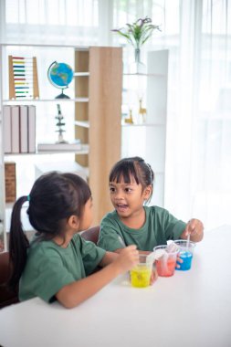 İki genç kız bir masada oturuyor, bir bilim deneyiyle oynuyorlar. Gülümsüyorlar ve eğleniyor gibiler.