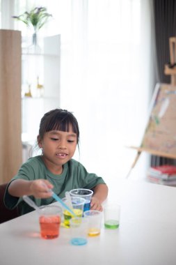 İki genç kız bir masada oturuyor, bir bilim deneyiyle oynuyorlar. Gülümsüyorlar ve eğleniyor gibiler.