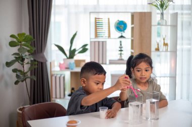 İki çocuk su ve yumurtalarla ilgili bir bilim deneyiyle oynuyorlar. Kadehleri tuzlamak için kaşık kullanıyorlar.