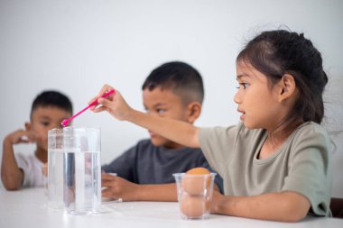 İki çocuk su ve yumurtalarla ilgili bir bilim deneyiyle oynuyorlar. Kadehleri tuzlamak için kaşık kullanıyorlar.