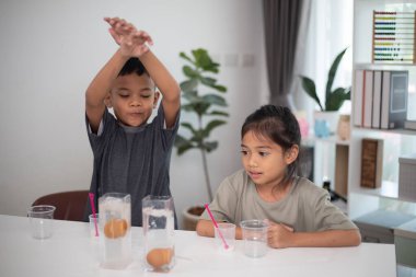 İki çocuk su ve yumurtalarla ilgili bir bilim deneyiyle oynuyorlar. Kadehleri tuzlamak için kaşık kullanıyorlar.