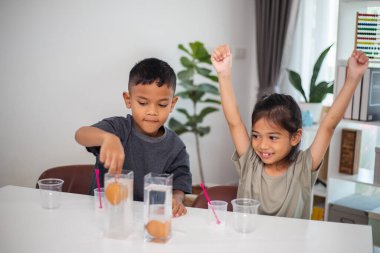 İki çocuk su ve yumurtalarla ilgili bir bilim deneyiyle oynuyorlar. Kadehleri tuzlamak için kaşık kullanıyorlar.