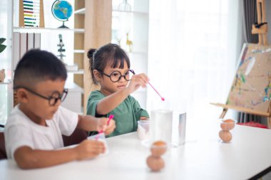 İki çocuk su ve yumurtalarla ilgili bir bilim deneyiyle oynuyorlar. Kadehleri tuzlamak için kaşık kullanıyorlar.