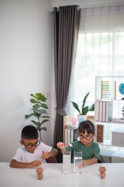 İki çocuk su ve yumurtalarla ilgili bir bilim deneyiyle oynuyorlar. Kadehleri tuzlamak için kaşık kullanıyorlar.