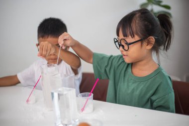 İki çocuk su ve yumurtalarla ilgili bir bilim deneyiyle oynuyorlar. Kadehleri tuzlamak için kaşık kullanıyorlar.