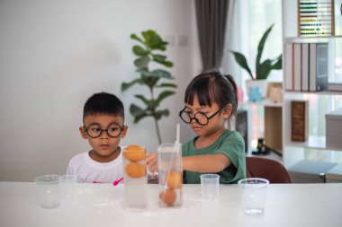 İki çocuk su ve yumurtalarla ilgili bir bilim deneyiyle oynuyorlar. Kadehleri tuzlamak için kaşık kullanıyorlar.