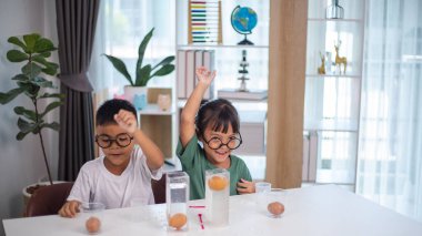 İki çocuk su ve yumurtalarla ilgili bir bilim deneyiyle oynuyorlar. Kadehleri tuzlamak için kaşık kullanıyorlar.