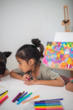 İki genç kız kalemler ve boyama kitaplarıyla bir masada oturuyorlar. Gülümsüyorlar ve eğleniyor gibi görünüyorlar. Kızlar çizim yaparken oyunculuk ve yaratıcılık kavramı