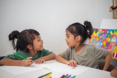 İki genç kız kalemler ve boyama kitaplarıyla bir masada oturuyorlar. Gülümsüyorlar ve eğleniyor gibi görünüyorlar. Kızlar çizim yaparken oyunculuk ve yaratıcılık kavramı