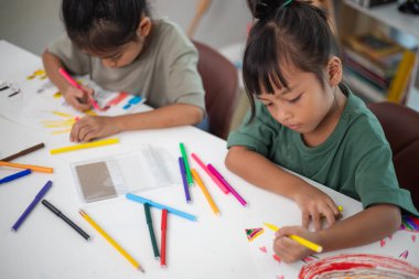 İki genç kız kalemler ve boyama kitaplarıyla bir masada oturuyorlar. Gülümsüyorlar ve eğleniyor gibi görünüyorlar. Kızlar çizim yaparken oyunculuk ve yaratıcılık kavramı
