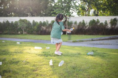 Genç kızlar parktan çöp topluyor. Ellerinde plastik şişeler ve bir çöp torbası var. Kızlar parkı temiz tutmak için harekete geçerken sahne olumlu ve umut verici.