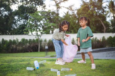 İki genç kız parkta çöp topluyor. Ellerinde plastik şişeler ve bir çöp torbası var. Kızlar parkı temiz tutmak için harekete geçerken sahne olumlu ve umut verici.