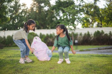 İki genç kız parkta çöp topluyor. Ellerinde plastik şişeler ve bir çöp torbası var. Kızlar parkı temiz tutmak için harekete geçerken sahne olumlu ve umut verici.