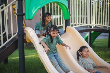 Üç genç kız parktaki sarı kaydırak.