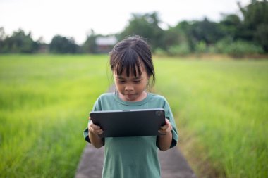 Genç bir kız tarlada bir tablet tutuyor. O ciddi bir ifadeyle ekrana bakıyor.