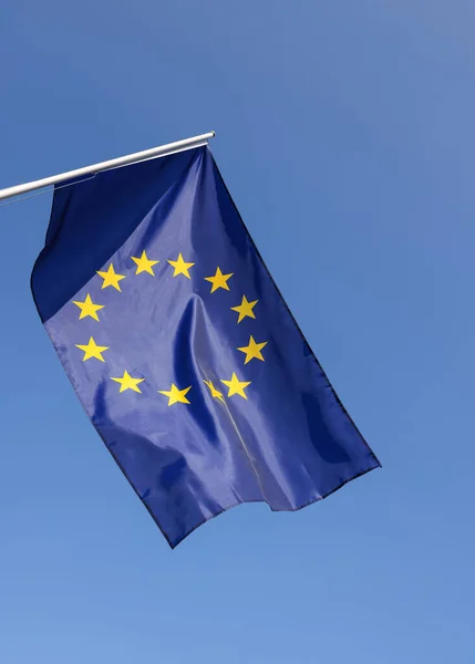 stock image European Union EU flag hanging on flagstaff over clear blue sky, symbol of European patriotism, low angle, side view