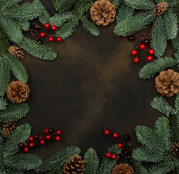 新鮮な緑のトウヒの国境フレームを閉じますコーンと赤いホリーベリーの装飾を持つクリスマスツリーの枝 コピースペースを持つ暗褐色の背景上 — ストック写真