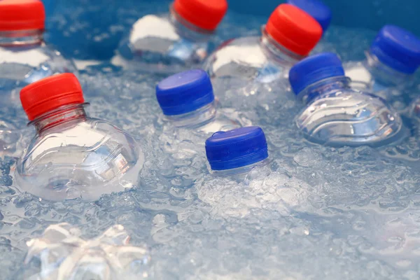 PET plastic bottles of cold still and sparking drinking mineral water with blue and red caps float and chill down in ice and water on retail market display, close up, high angle view