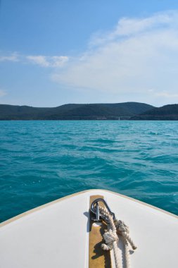 Yelkenli mavi deniz veya göl suyu, beyaz tekne yayı üzerinden görüş, ufuktaki dağlar, seyahat ve seyahat konsepti, kişisel bakış açısı, kopyalama alanı