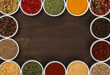 Beyaz seramik kâselerdeki çeşitli baharatların çerçevesi koyu ahşap masa arkaplanının üzerinde fotokopi alanı, yüksek üst manzara, tam üstte.