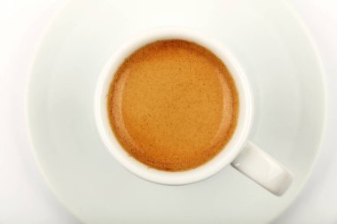 Kahverengi kremalı espresso dolu beyaz bardak, çay tabağı, beyaz arka plan, üst manzara, tam üstte.