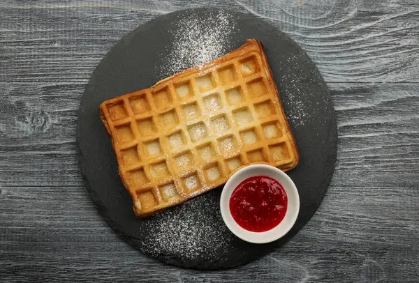 Büyük, geleneksel Amerikan ya da Belçika waffle 'ını pudra şekeri ve ahududu reçeli ile kapatıyoruz. Masadaki siyah tahtada servis ediliyor.