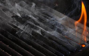 Close up empty cast iron metal BBQ grill grate with fire flames and smoke, hot charcoal below, high angle view
