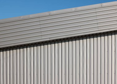 Boyanmamış gri alüminyumun arkaplan dokusu mavi gökyüzünün altında kepekli metal duvar