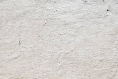 Beyaz boyanmış beton bir duvar yüzeyinin yakın görüntüsü, görünür fırça darbelerini ve çatlakları ortaya çıkarıyor, desenli ve yıpranmış bir zemin oluşturuyor