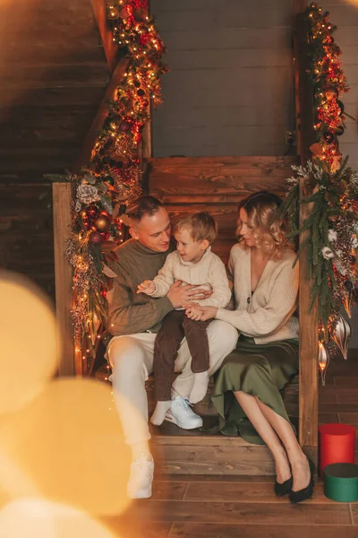サンタ屋内を待っているニットベージュのセーターで幸せな家族の肖像画 笑顔の両親抱擁とキス彼の小さな息子Eve 12月はガーランドライトでクリスマスを祝う Noel Tree Gift Giving — ストック写真