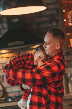 Kırmızı kareli elbiseli, Noel Baba 'yı evde bekleyen küçük oğlu olan aktif ailelere gülümseyin. Tarz sahibi aile, gülüşlere, kucaklaşmalara evde sarılmaya bayılır. 25 Aralık Noel Ağacı 'nın yeni yıl çelenkleri ve ışıkları kutlanır