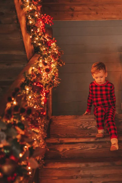 Smile small child being active having fun in motion and waiting for miracle Santa. Red checkered sleepwear kid playing indulge indoor jumping moving laughing garlands lights Noel tree eve 25 December