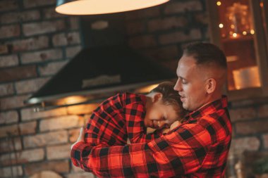 Kırmızı kareli elbiseli, Noel Baba 'yı evde bekleyen küçük oğlu olan aktif ailelere gülümseyin. Tarz sahibi aile, gülüşlere, kucaklaşmalara evde sarılmaya bayılır. 25 Aralık Noel Ağacı 'nın yeni yıl çelenkleri ve ışıkları kutlanır