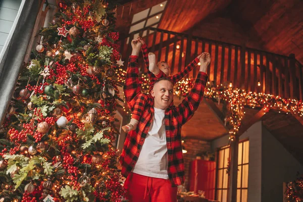 笑顔の小さな男の子がお互いの屋内待っている奇跡と楽しんで父親の首に座っています ノエルの木の冬の季節のガーランドライトで新年を祝うクリスマスの精神前夜25 12月父方の愛 ロイヤリティフリーのストック画像