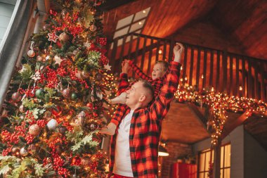 Gülümse küçük çocuk, babanın boynuna oturup içeride eğleniyor ve mucize bekliyor. Noel ağacı kış sezonunun çelenk ışıklarıyla yeni yılı kutluyoruz Noel ruhu 25 Aralık baba sevgisi arifesi