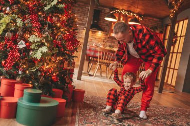 Gülümse küçük çocuk, babanın boynuna oturup içeride eğleniyor ve mucize bekliyor. Noel ağacı kış sezonunun çelenk ışıklarıyla yeni yılı kutluyoruz Noel ruhu 25 Aralık baba sevgisi arifesi