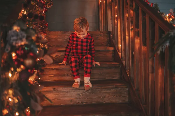 Smile small child being active having fun in motion and waiting for miracle Santa. Red checkered sleepwear kid playing indulge indoor jumping moving laughing garlands lights Noel tree eve 25 December