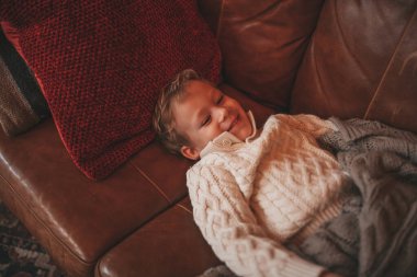 Gülümse küçük çocuk hareket halinde eğleniyor ve hayalperest mucize Noel Baba 'yı bekliyor. 25 Aralık 'ın arifesinde, kanepede örgü kıyafetli, oyuncaklarla oynayan neşeli çocuk Noel.