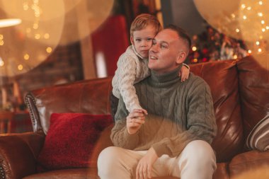 Gülümse küçük çocuk ve baba içeride Noel Baba 'yı beklerken kucaklaşıp öpüşüyorlar. Noel ağacı kış sezonunun çelenk ışıklarıyla yeni yılı kutluyoruz Noel ruhu 25 Aralık baba sevgisi arifesi