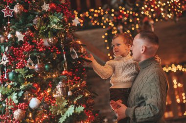 Gülümse küçük çocuk ve baba içeride Noel Baba 'yı beklerken kucaklaşıp öpüşüyorlar. Noel ağacı kış sezonunun çelenk ışıklarıyla yeni yılı kutluyoruz Noel ruhu 25 Aralık baba sevgisi arifesi